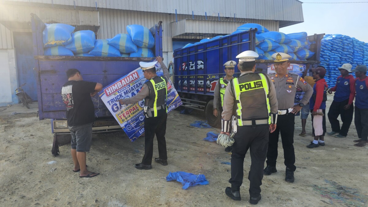 Foto : Personel Satlantas Polres Pamekasan memasang spanduk imbauan kepada sopir truk angkutan garam di area Gudang Garam, Desa Majungan, Kecamatan Pademawu, Kabupaten Pamekasan, Kamis (27/8/2026). Imbauan terkait penutupan muatan dengan terpal untuk mengantisipasi jalan licin akibat tetesan air garam.